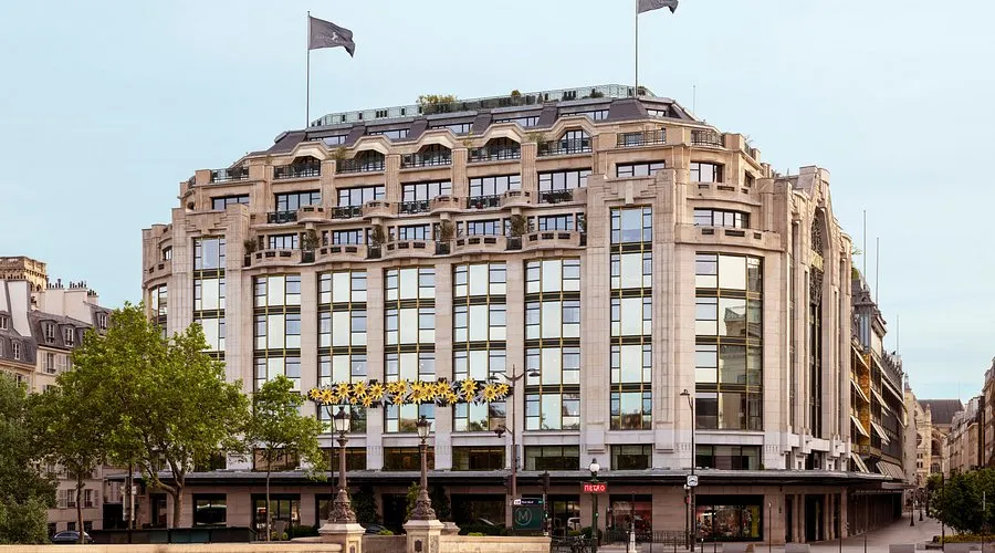 Cheval Blanc Paris in La Samaritaine: a cream-stone building of stepped storeys and tall windows above the trees of the quay, two flags on its roof