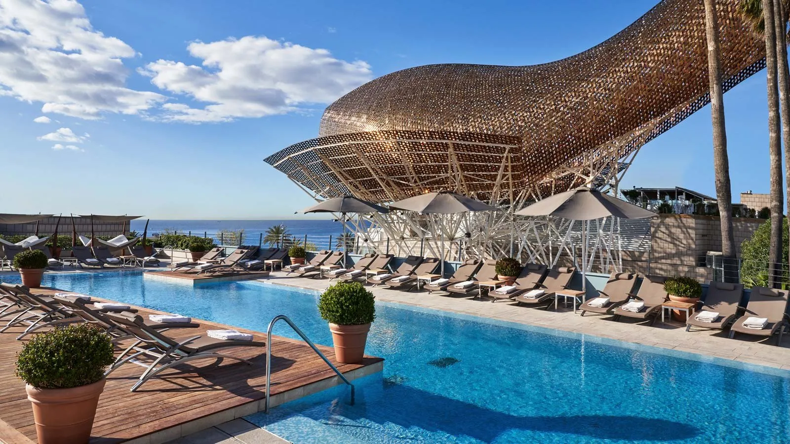 An outdoor pool at Hotel Arts, with loungers along it and Frank Gehry's gold fish sculpture above