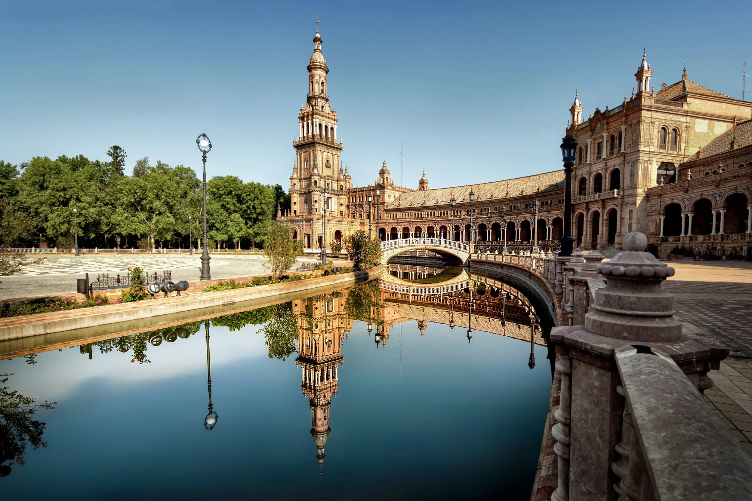 The Plaza de España in Seville at first light, its north tower and tiled bridge mirrored in the still canal